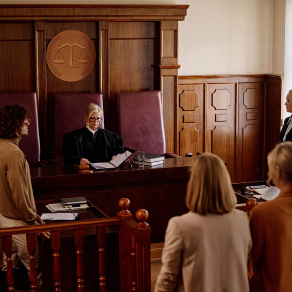Group of witnesses, attorneys, prosecutor and suspect standing in courtroom Group of witnesses, attorneys, lawyers, prosecutor and suspect standing in front of experienced blond female judge in mantle passing judgement